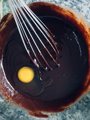 the cake mixture for chocolate brownies in a bowl whisking in an egg
